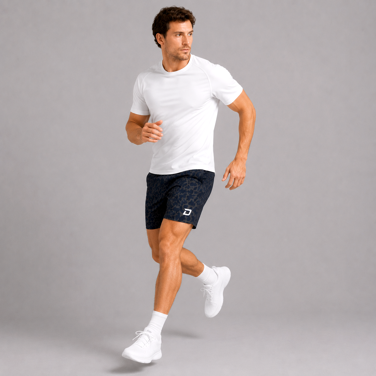 Male model in motion wearing Midnight Performance Shorts with a subtle dark pattern, paired with a white performance tee and white sneakers in a clean studio setting that highlights lightweight comfort and unrestricted movement.
