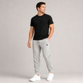 Male model wearing the Dink Air Classic Joggers in gray featuring an embroidered black D Mark logo, tapered athletic fit, lightweight performance fabric, elastic waistband, ribbed ankle cuffs, and a clean minimalist design for pickleball, training, travel, recovery, and everyday wear.