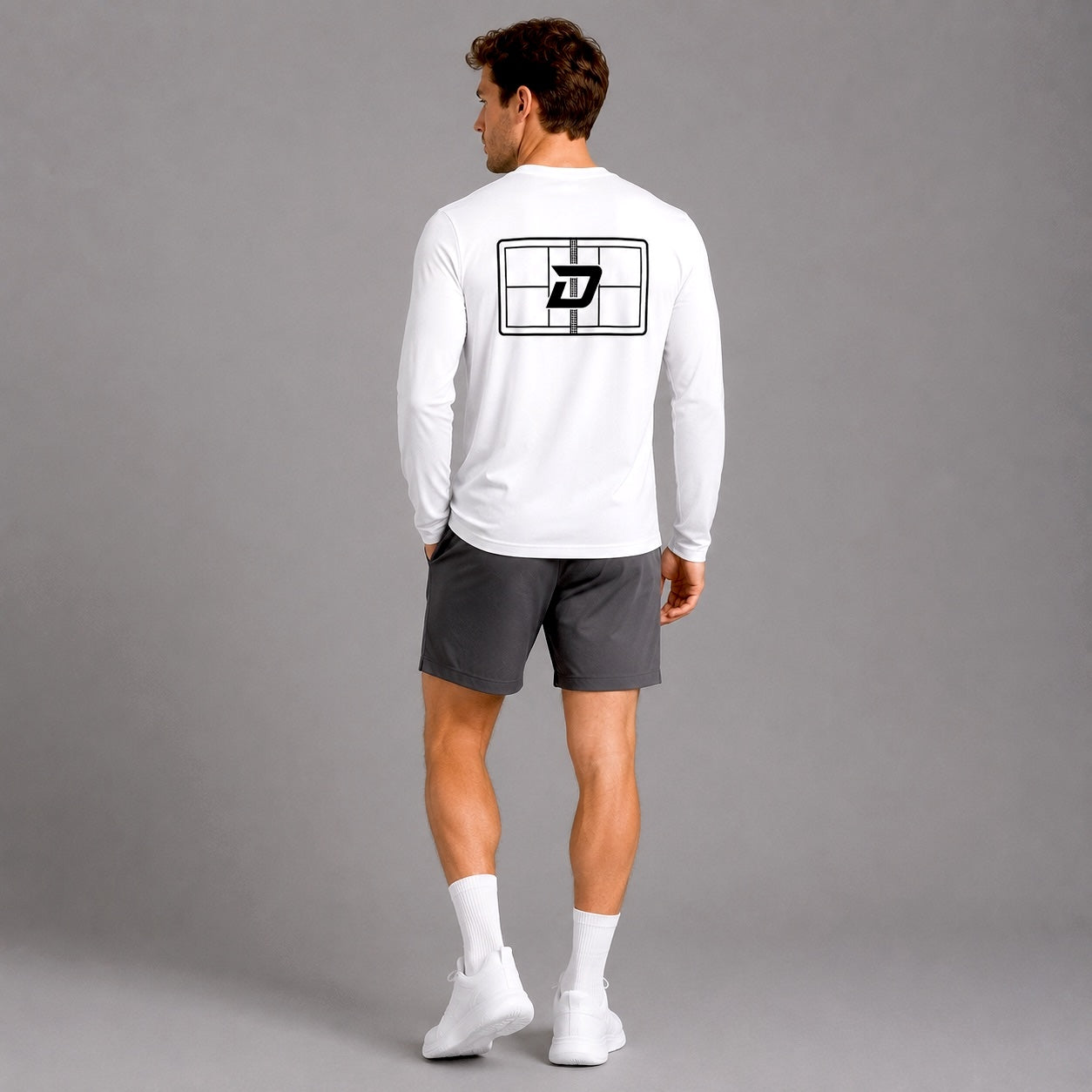 Male model wearing the white Court Long Sleeve Tee featuring the signature D Mark court graphic on the back, paired with charcoal performance shorts in a studio lifestyle setting.
