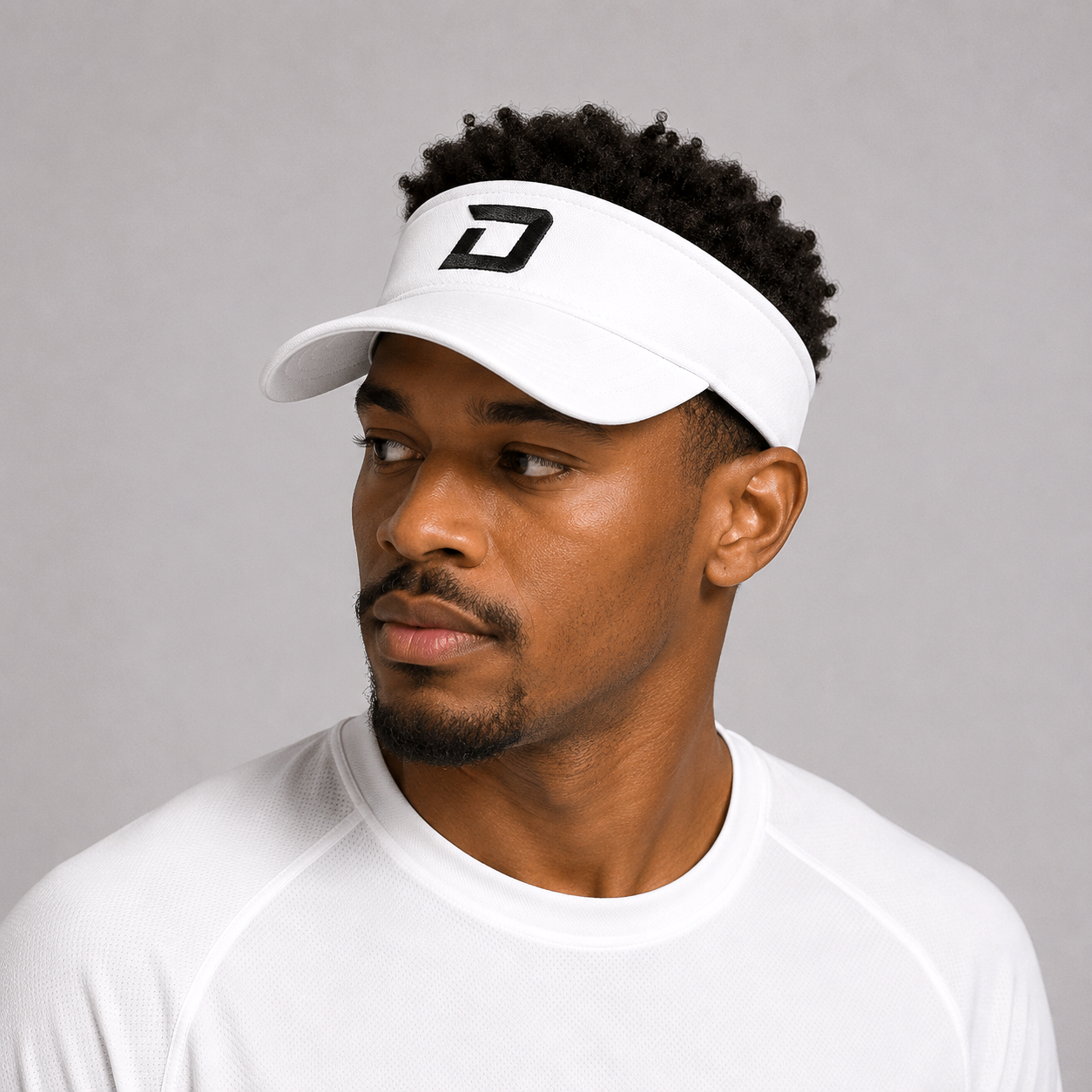 Male model wearing the white D Mark Performance Visor with a white athletic tee, showcasing the embroidered black D logo and lightweight design built for comfort and sun protection on and off the pickleball court.