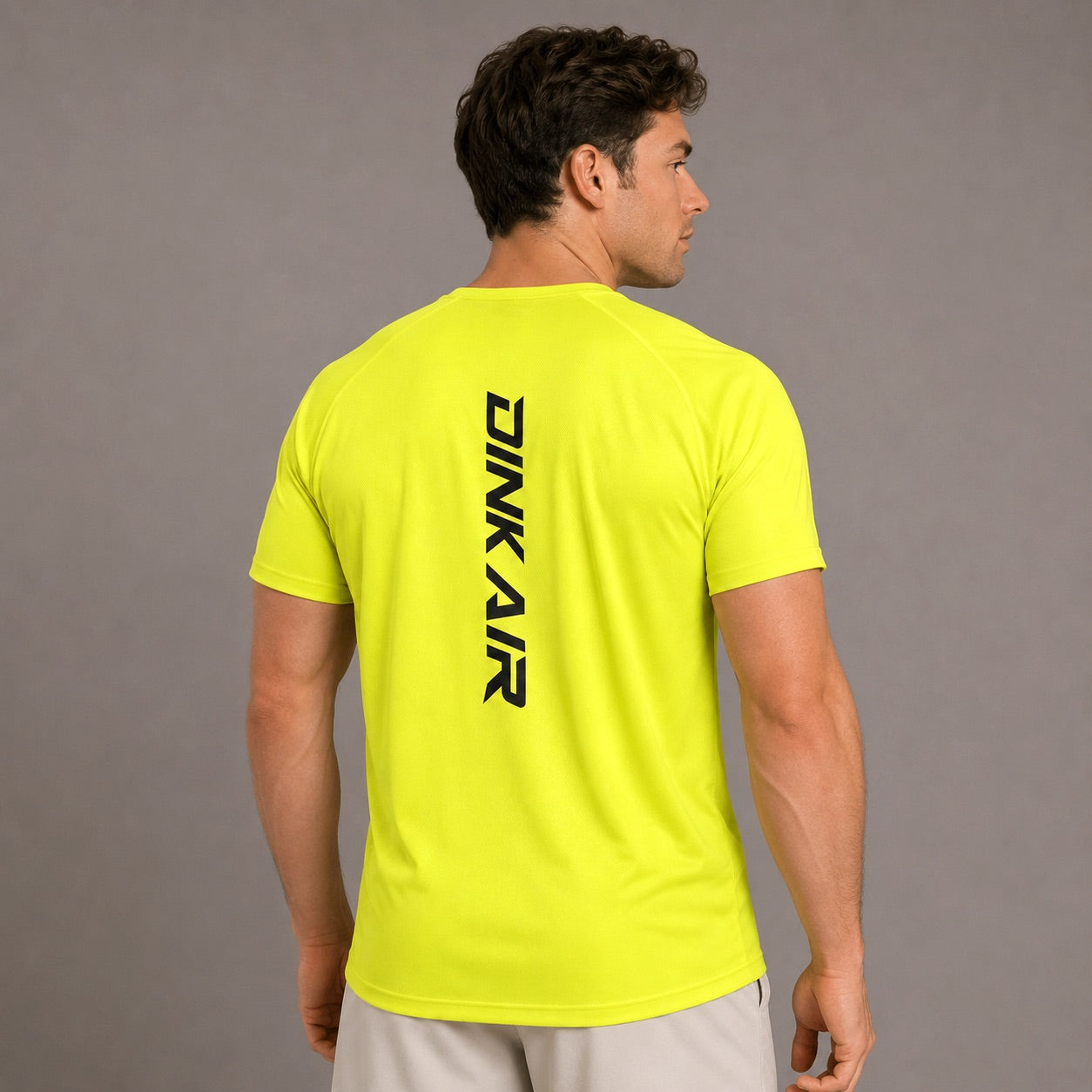 Male model wearing the Dink Air Vertical Performance Tee in neon yellow, shown from the back with the vertical black Dink Air logo in a neutral studio setting.