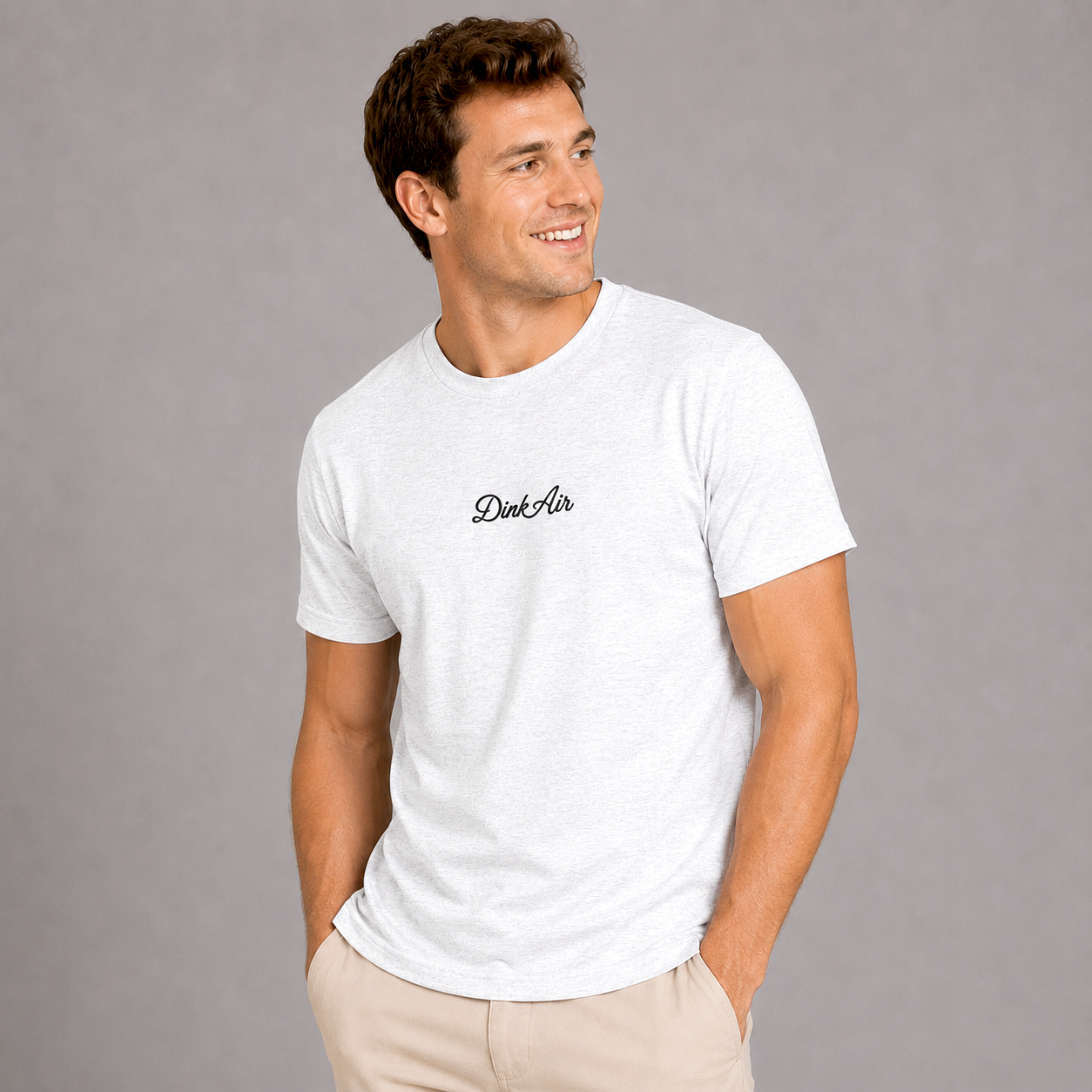 Male model wearing the Dink Air Signature Script Tee featuring premium embroidered Dink Air script on a white tri-blend t-shirt, paired with light khaki pants in a clean studio setting that highlights the shirt's soft comfort, premium fit, and timeless everyday style.