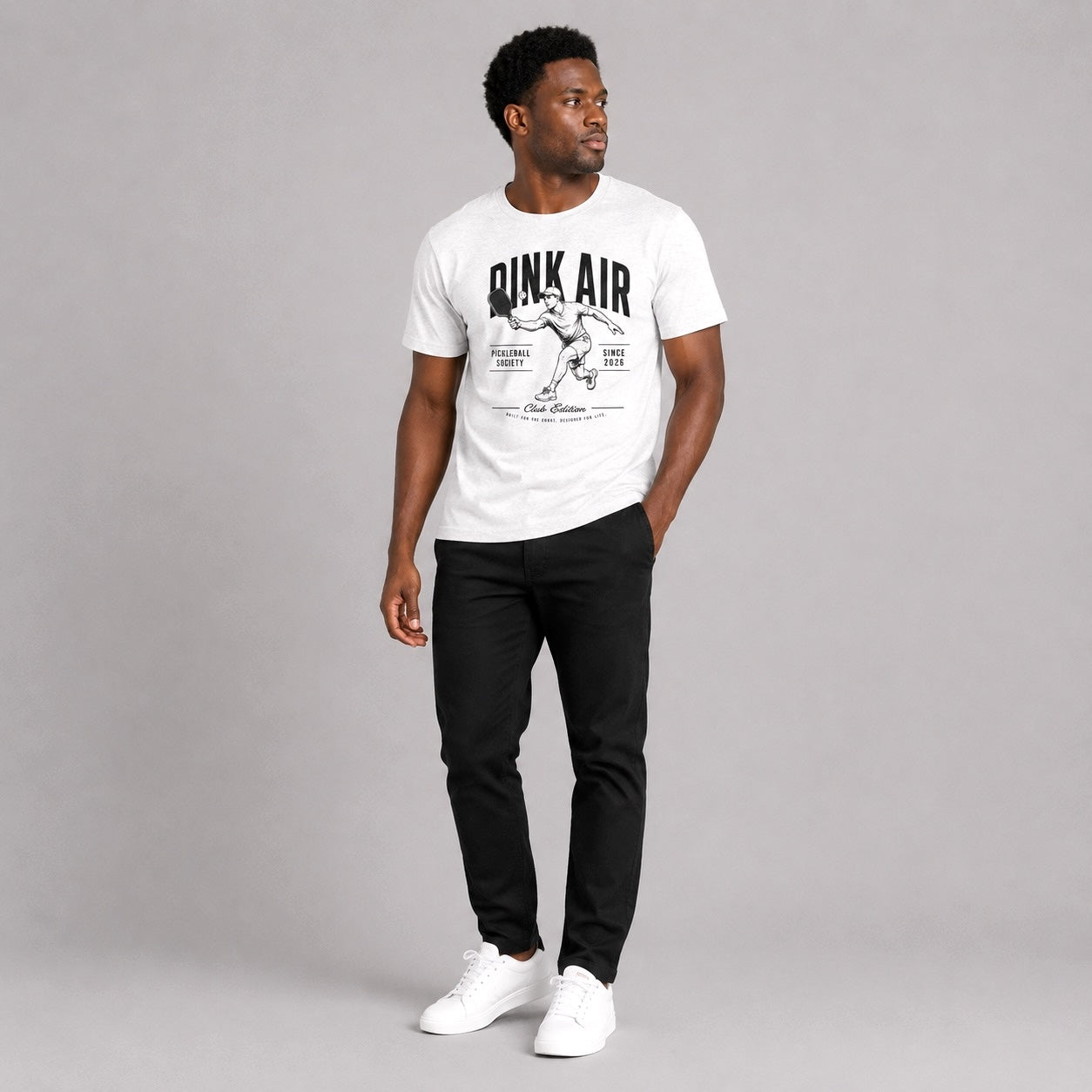 Male model wearing the white Originals Match Tee with a vintage-inspired pickleball graphic, styled with black pants in a casual lifestyle setting.