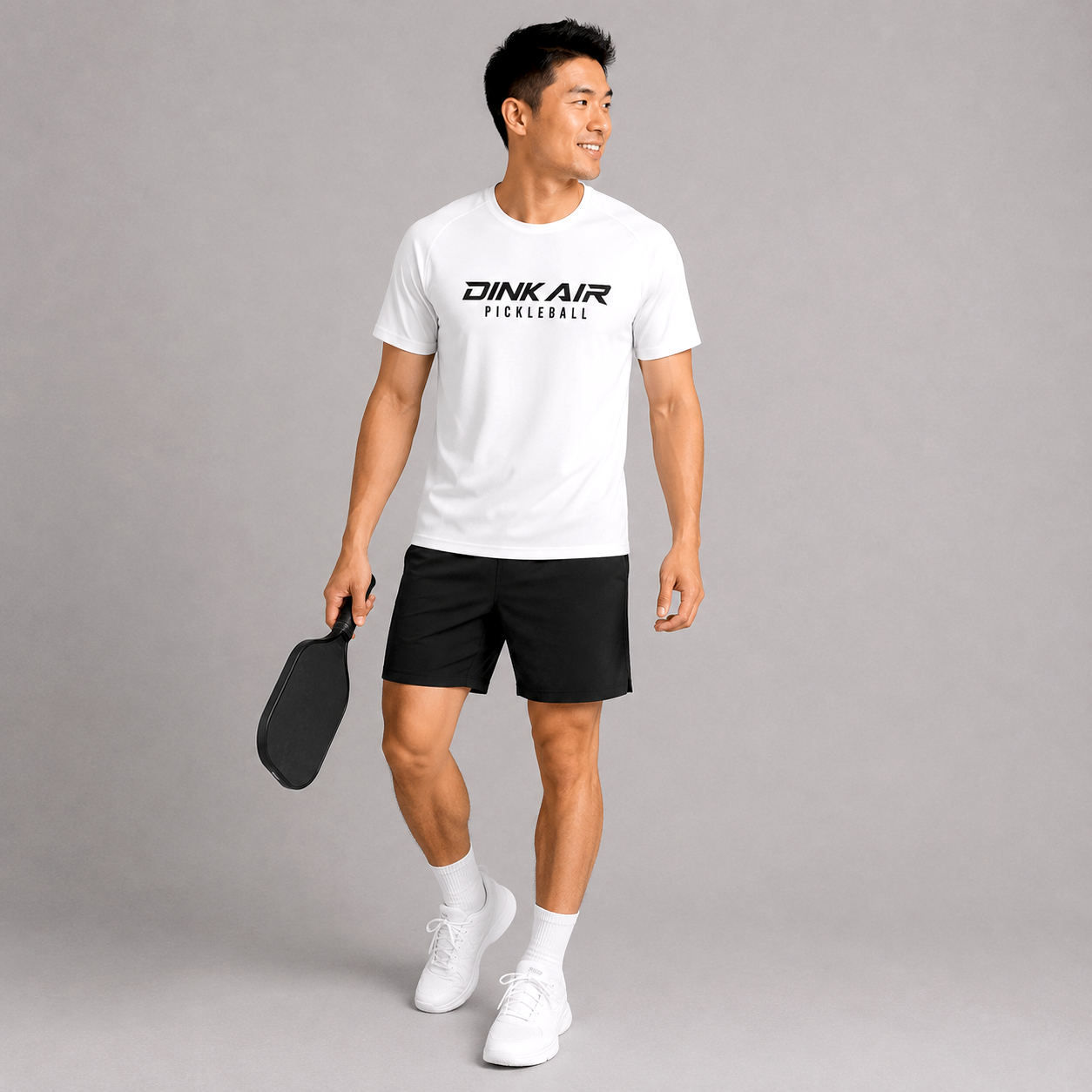Athletic male model wearing the white Signature Pickleball Performance Tee with black performance shorts, showcasing the bold Dink Air Pickleball logo on a lightweight moisture-wicking shirt designed for comfort and movement on and off the court.